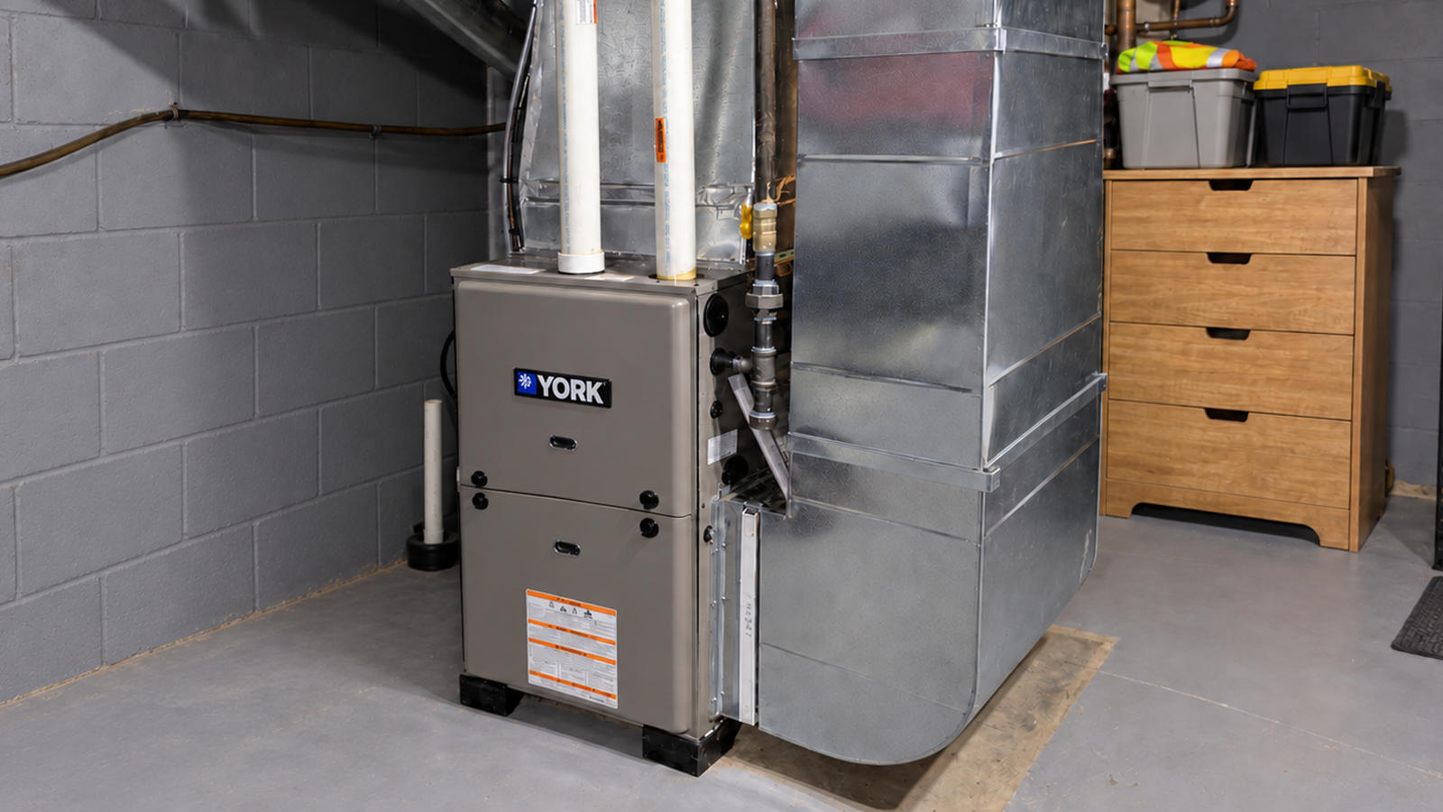 A modern York gas furnace installed in a basement basement utility room connected to sheet metal ductwork.